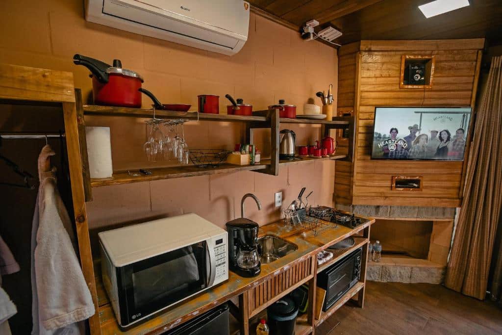 cozinha equipada do Sunset Serrano Chalés com micro-ondas, panelas, fogão de indução, pia e demais utensilhos, há ainda ar-condicionado e tv que podem ser vistas no interior do ambiente.