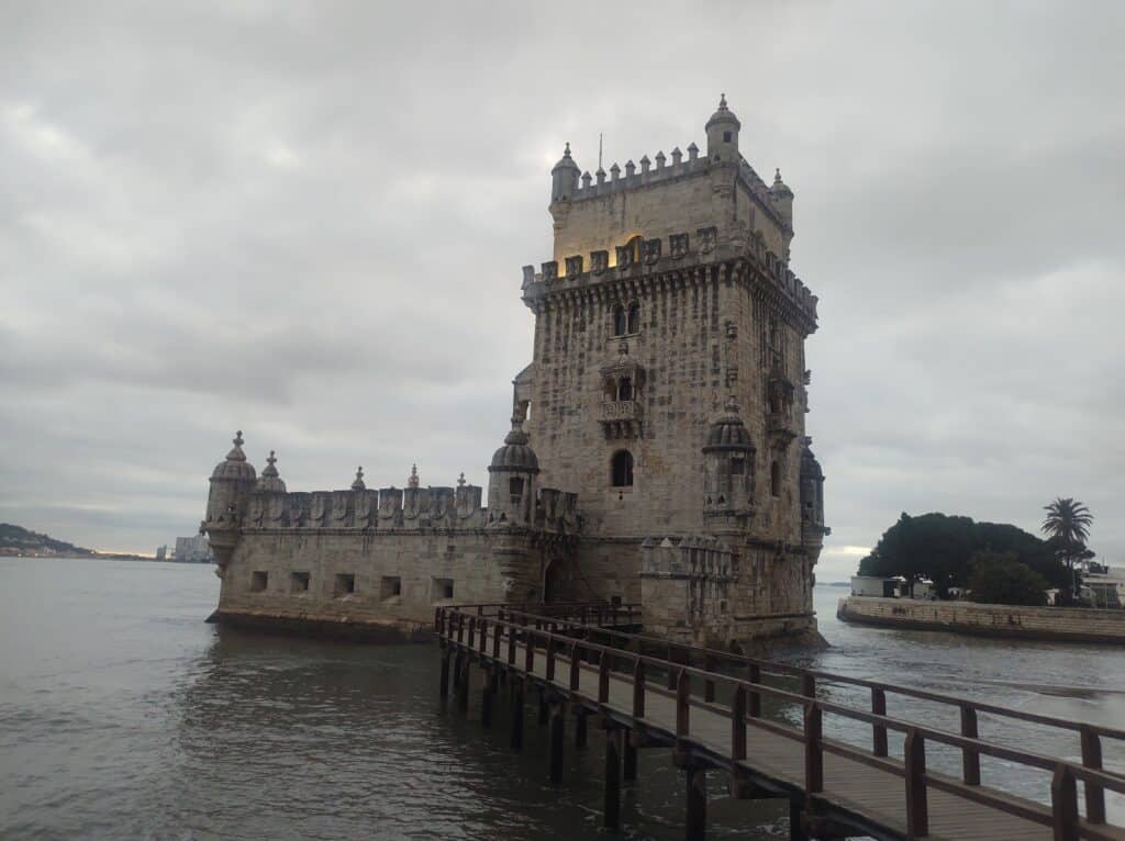 Imagem da Torre de Belém durante o final do dia com uma ponte do lado direito com um rio abaixo e a torre do lado direito. Representa o que fazer em Lisboa.