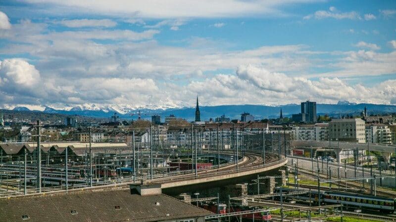 Imagem durante o dia da vista de Zurique da Loja Freitag com imagem de uma ponte no centro e ao fundo edifícios. Representa o que fazer em Zurique.