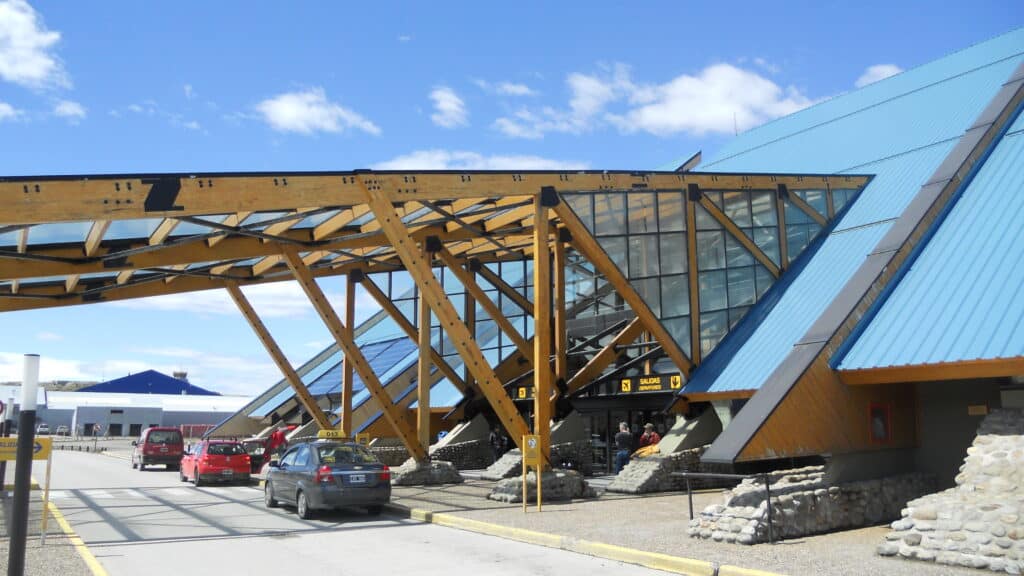 Aeroporto de Ushuaia Malvinas Argentinas para ilustrar post sobre como chegar em Ushuaia. Uma rua com carros parados em frente a porta do aeroporto.