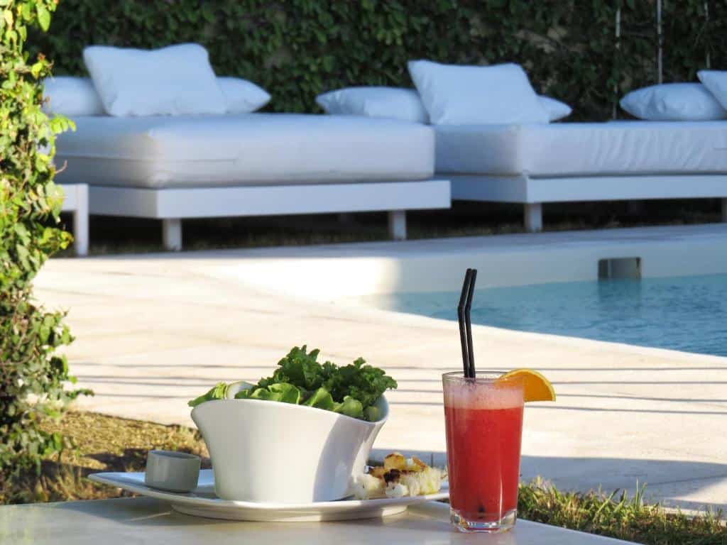 Uma tigela de salada e um drinque rosa estão em uma mesa ao lado de uma piscina, com espreguiçadeiras brancas ao fundo, no Atlántico Boutique Hotel (Península).
