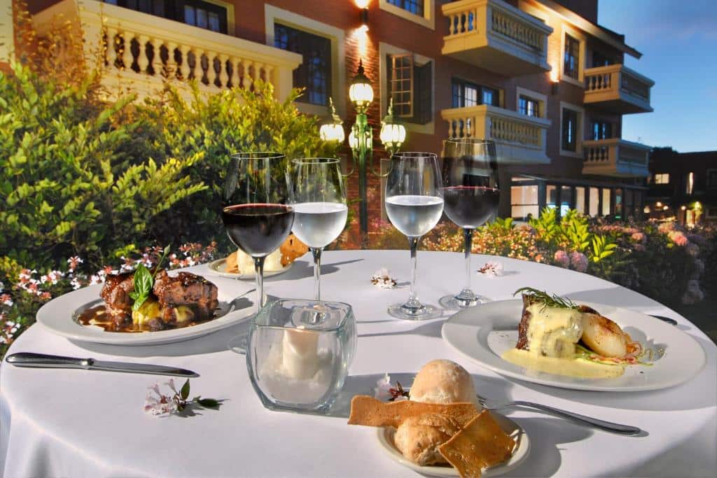 Uma mesa redonda ao ar livre com dois pratos de comida, copos de vinho e água, pãezinhos e uma vela, colocada perto de um edifício, no Barradas Parque Hotel & Spa.