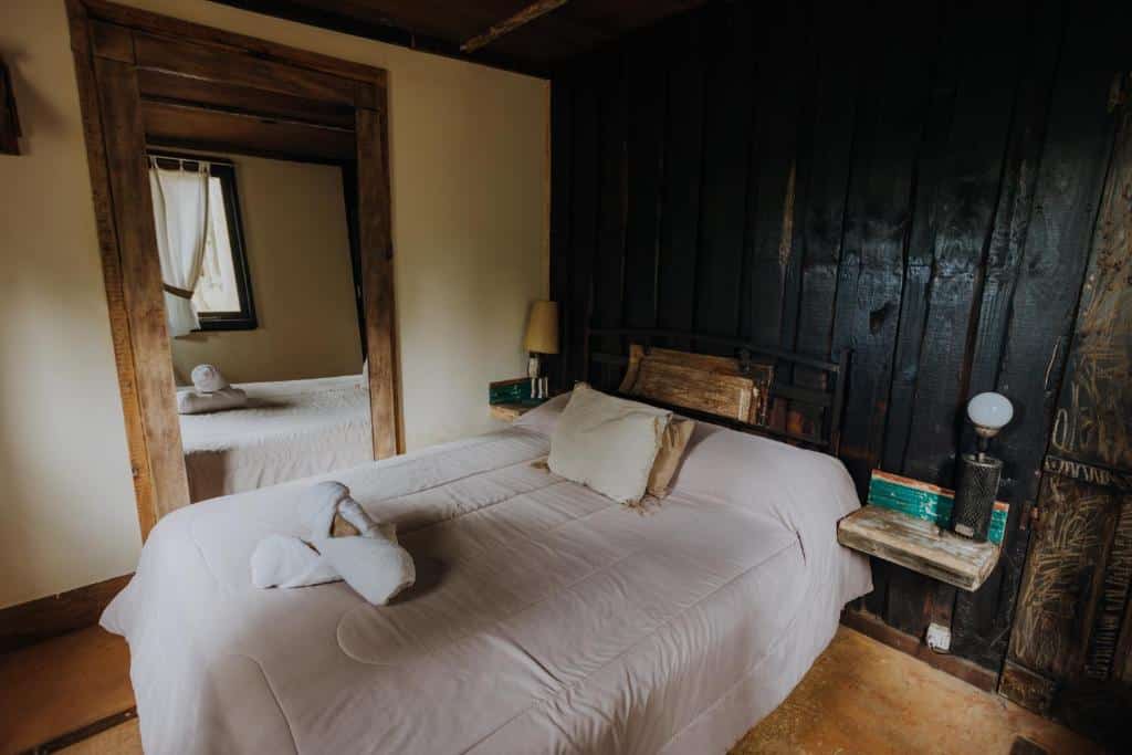 Um quarto rústico com uma cama de casal, roupa de cama branca, paredes de madeira, uma luminária de cabeceira e um grande espelho de parede, no Cabañas en el Bosque, para representar onde ficar em Punta del Este.