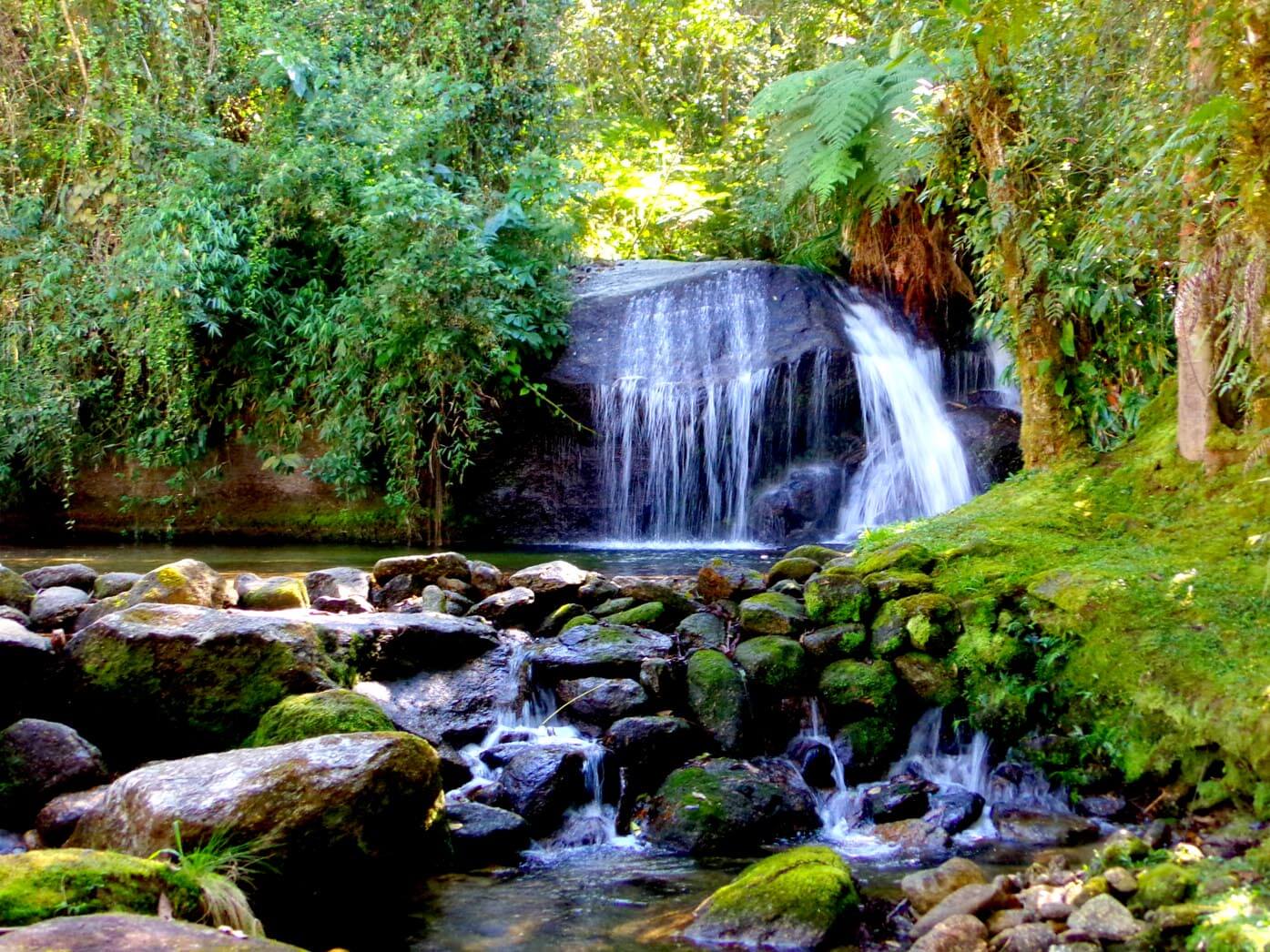Imagem da Cachoeirinha que faz parte do Sítio Cachoeiras do Alcantilado em Visconde de Mauá. O local tem várias pedras e árvores ao redor de uma pequena queda d'água. Imagem ilustrando post O que fazer em Visconde de Mauá.
