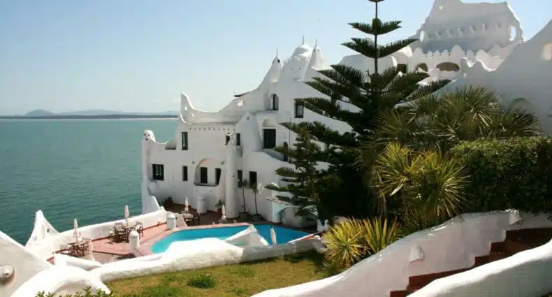 Foto aérea do Club Hotel Casapueblo em Punta Del Este, no Uruguai. Vê-se uma estrutura branca contemporânea, em meio à natureza e perto do mar.