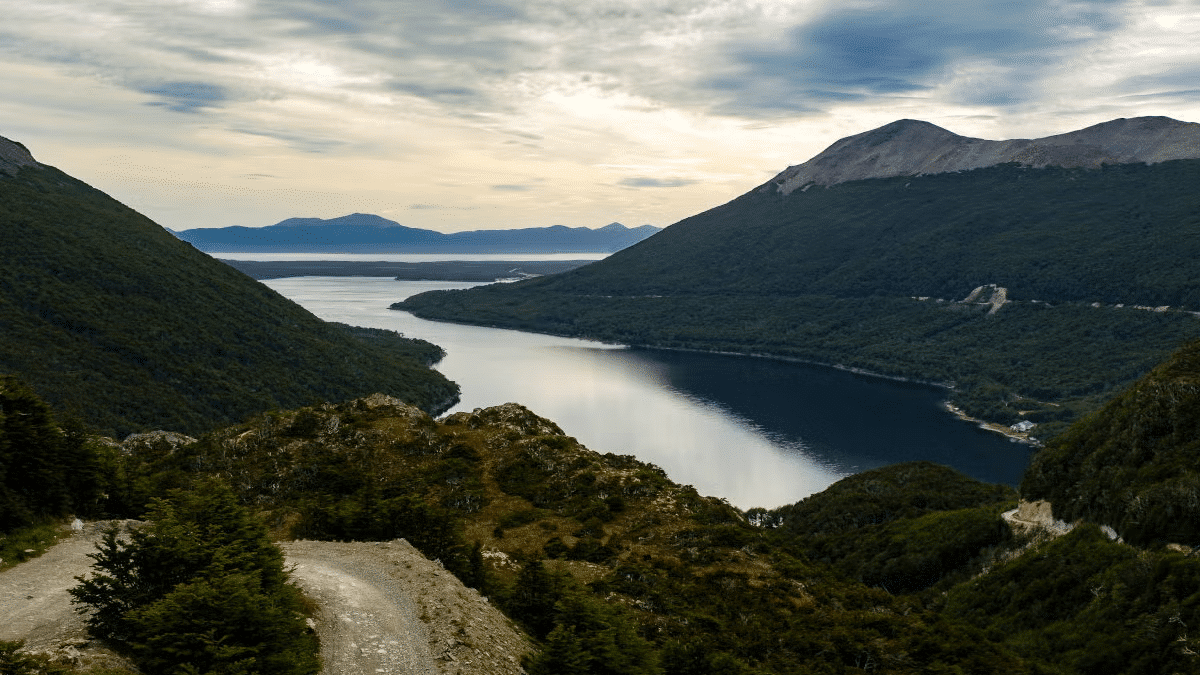 Uma estrada no canto esquerdo, no meio o lago escondido ao redor montanhas. Imagem para ilustrar post sobre passeios em Ushuaia.