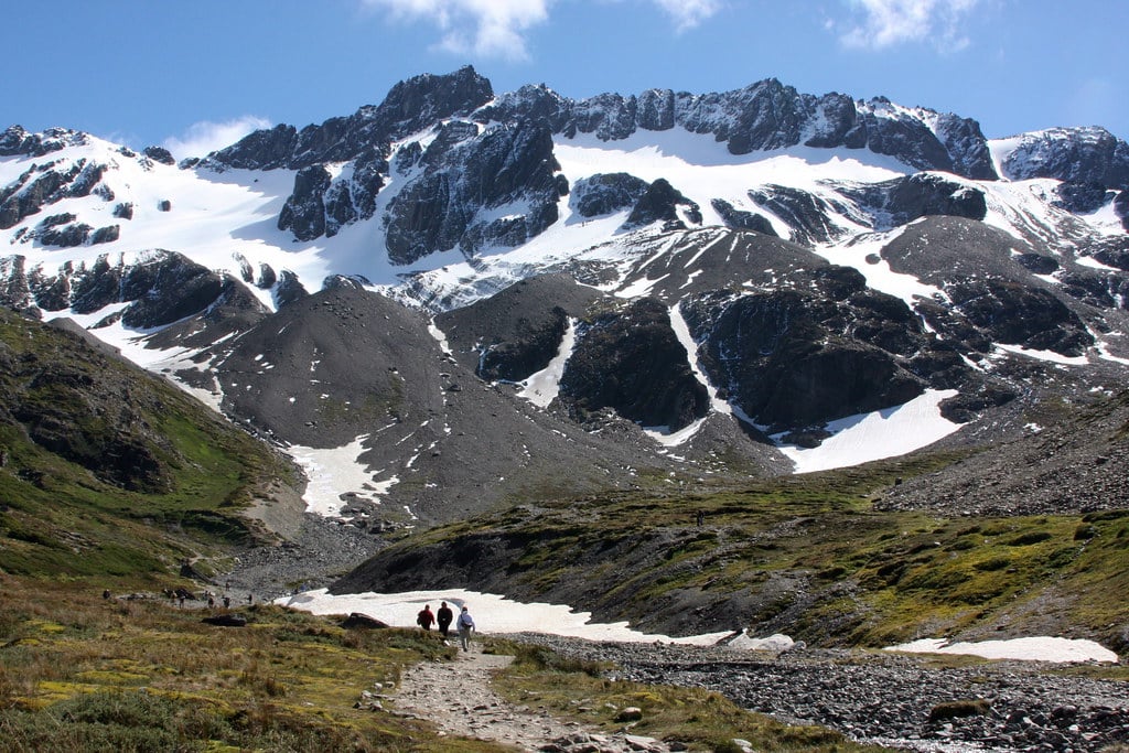 A trilha do Glaciar Martial com pessoas. No fundo as montanhas com neve.