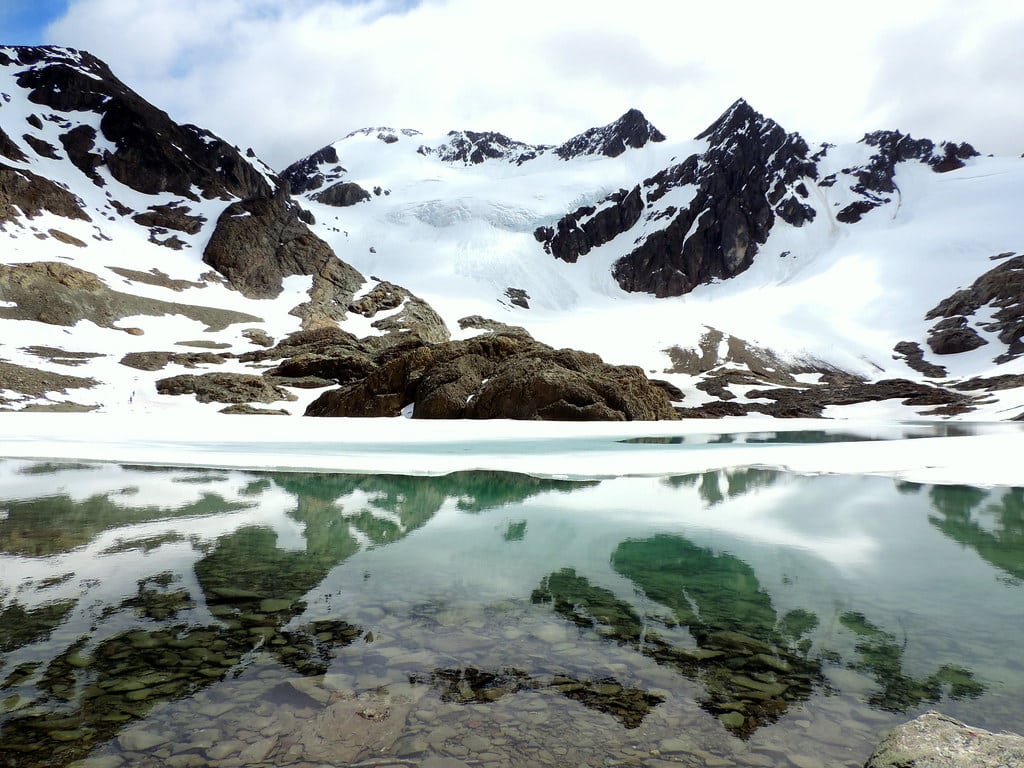O lago do Glaciar Vinciguerra na frente, atrás neve e montanhas com neves.