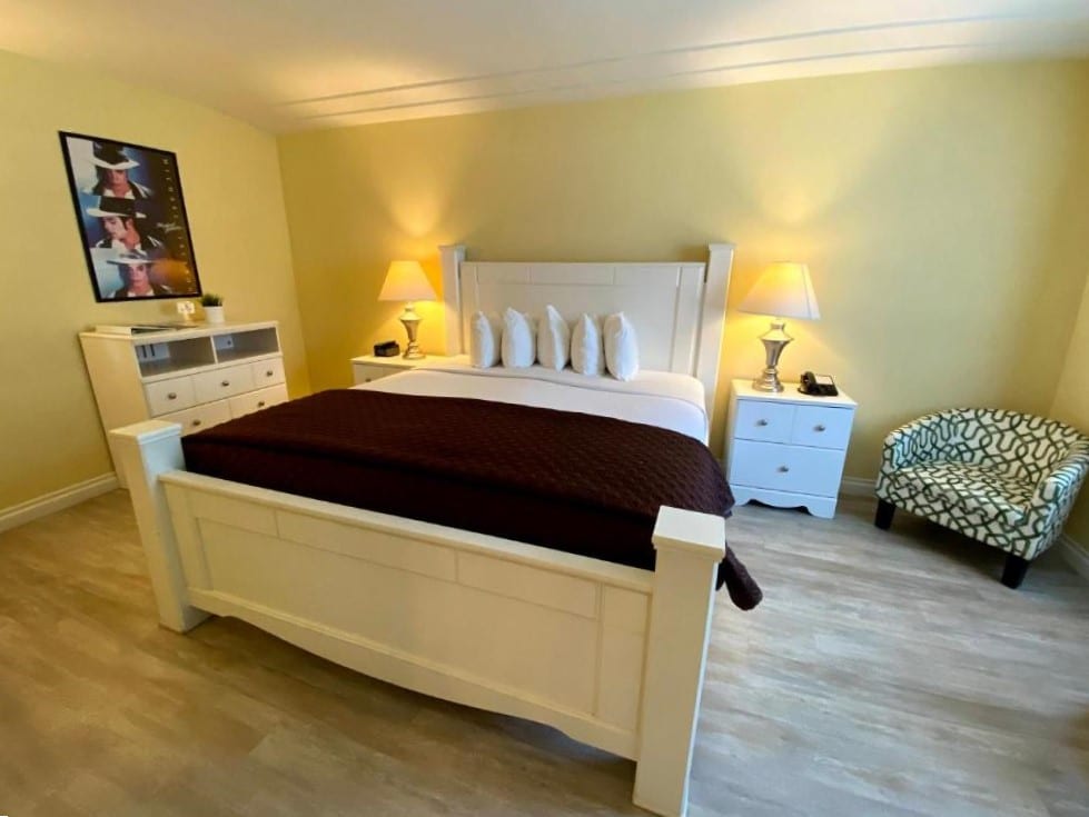 Quarto do Hollywood Celebrity Hotel. Uma cama de casal no centro, de cada lado uma cômoda co abajur. No canto direito uma poltrona, do lado esquerdo uma cômoda com um quadro. Foto para ilustrar post sobre hotéis baratos em Los Angeles.