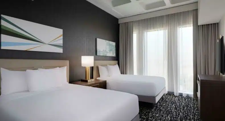 Quarto do Hyatt House LAX Century Blvs para ilustrar post sobre hotéis baratos em Los Angeles. Duas camas de casal do lado esquerdo, entre elas uma cômoda com abajur. Do lado direito uma cômoda com televisão. No fundo, uma cortina tampando a janela.
