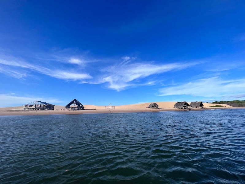Imagem das Ilha das Canárias durante o dia com um rio a frente e ao fundo dunas com barracas de palhas na borda do rio. Representa o que fazer no Delta do Parnaíba.
