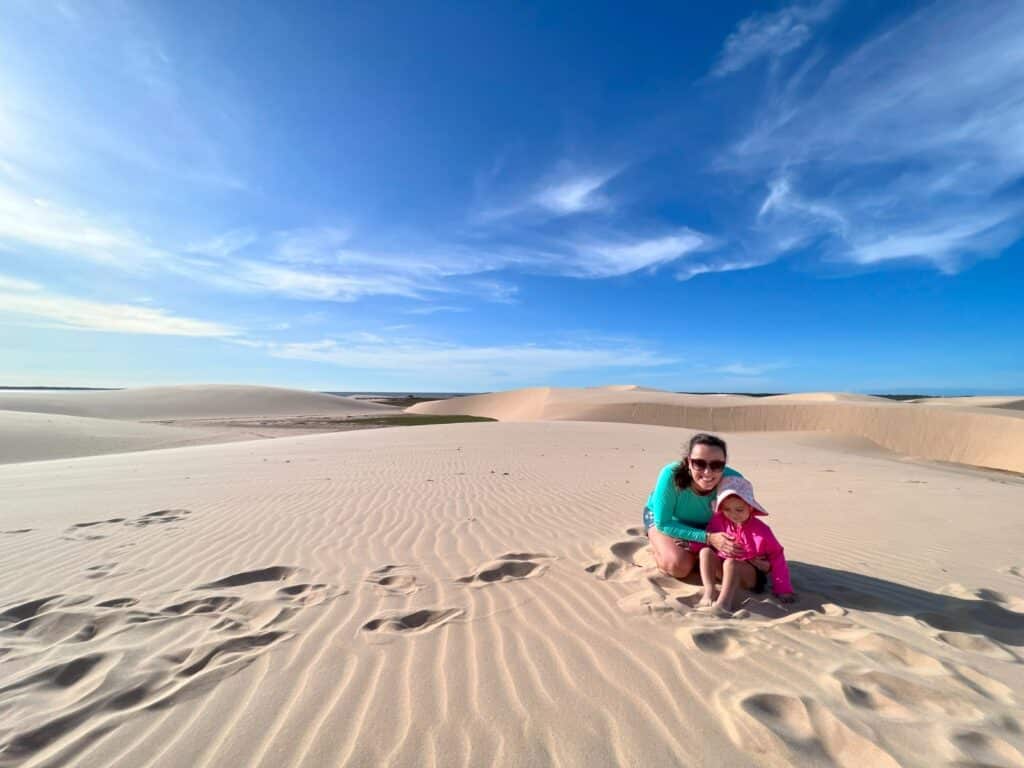 Imagem dos Lençóis Piauienses durante o dia com dunas de areia a frente uma mulher e uma criança do lado direito da imagem e ao fundo mais dunas de areia.
