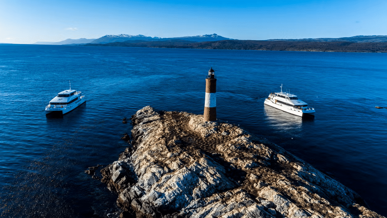 Vista de cima do Canal Beagle. Ao redor do farol o oceano e dois barcos. Imagem para ilustrar post sobre passeios em Ushuaia.