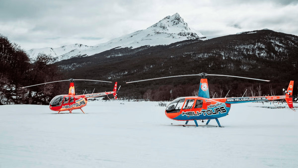 Dois helicópteros pousados na neve, no fundo as montanhas.