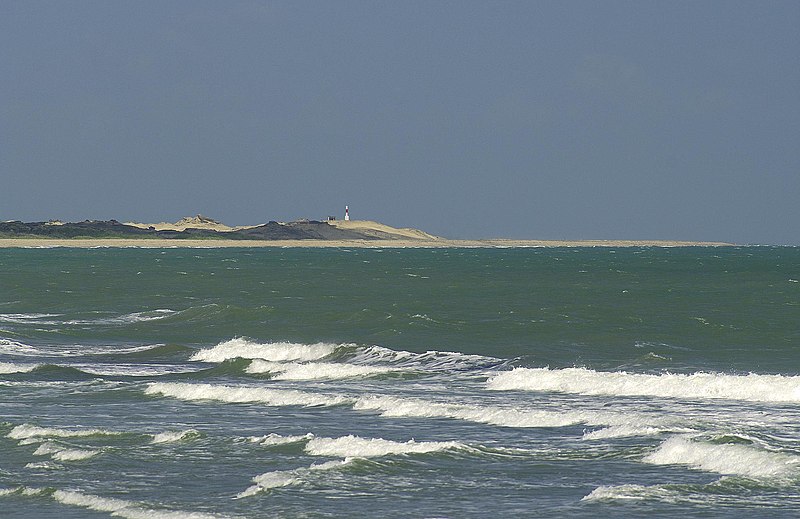 Imagem da praia da Atalaia durante o dia com mar a frente com ondas e ao fundo uma faixa de areia com farol.