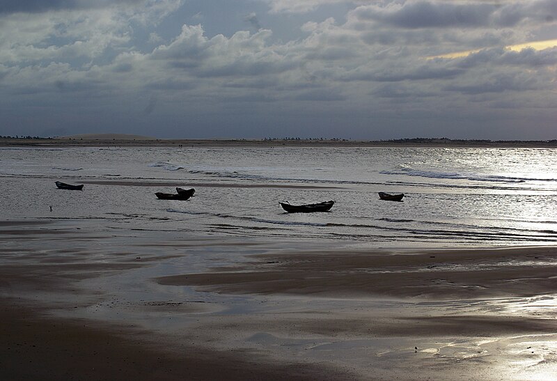 Imagem da praia Pedra do Sal no final do dia com areia a frente e ao fundo barcos dentro do mar.