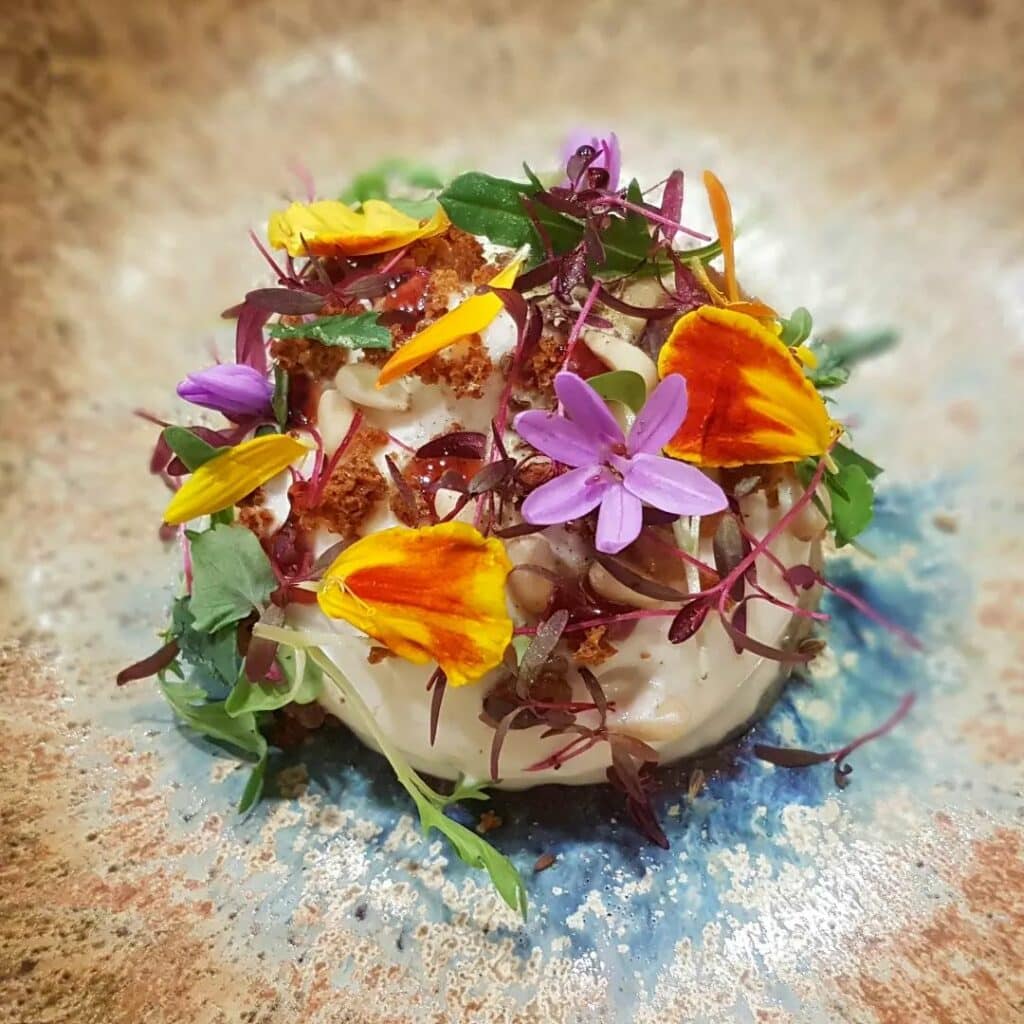 Imagem do prato Espírito de Garrigues
do Restaurant Hiely Lucullus com uma massa em baixo e folhas e flores em cima.