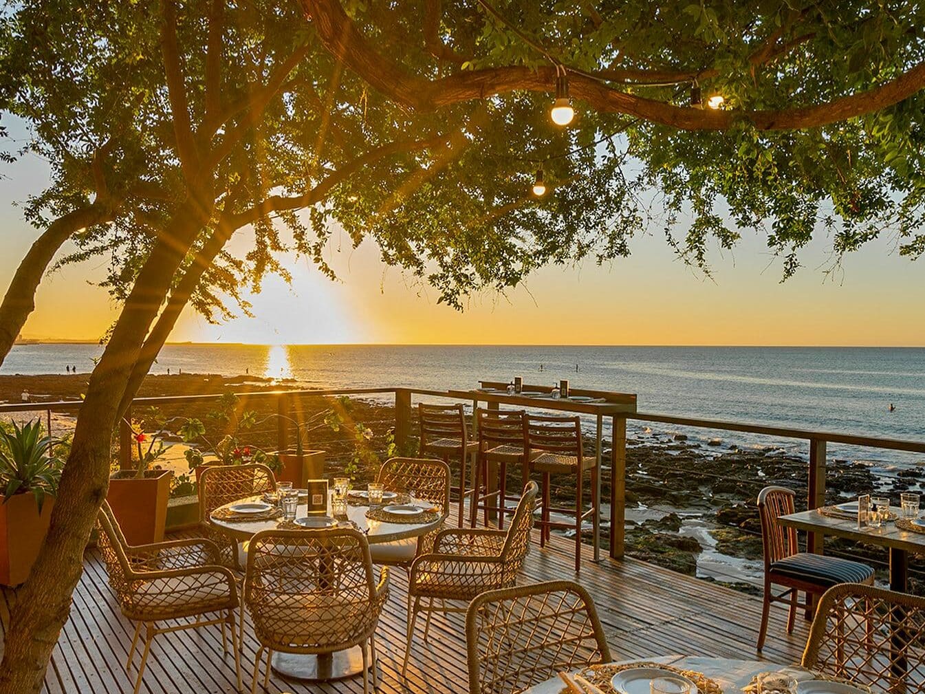 Foto de um deck do restaurante Illa Mare, com mesas e cadeiras voltadas para o mar. O sol se põe ao fundo.