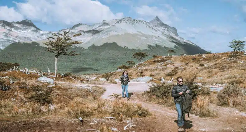 Duas pessoas fazendo a trilha na Laguna Esmeralda, no fundo montanhas. Imagem para ilustrar post sobre como chegar em Ushuaia.