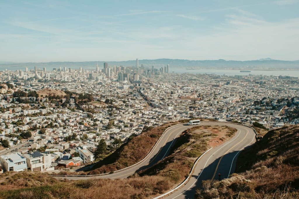 Foto do mirante Twin Peaks. Duas estradas iguais estão em uma montanha, formando quse um caminho em formato de U. Na ponta é possível ter uma visão panorâmica de San Francisco.