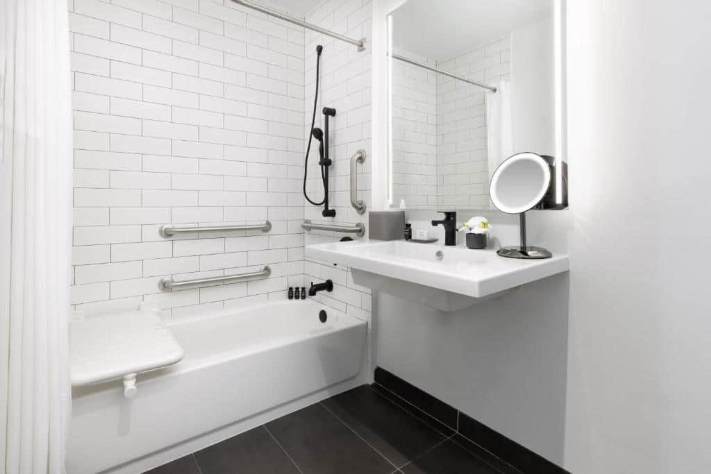 Banheiro com acessibilidade do The Elser Hotel Miami - An All-Suite Hotel com pia baixa do lado direito da imagem e do lado direito da pia banheira com barras de apoio.