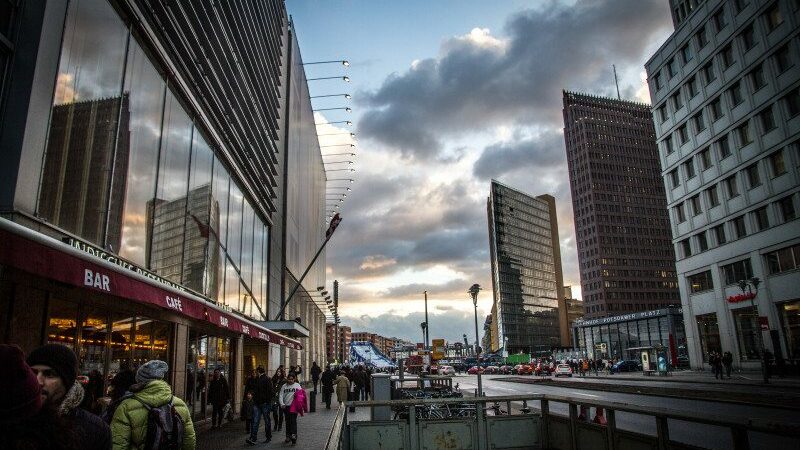 Imagem do Potsdamer durante o dia com prédios em cada lado da imagem e no centro pessoas andando.