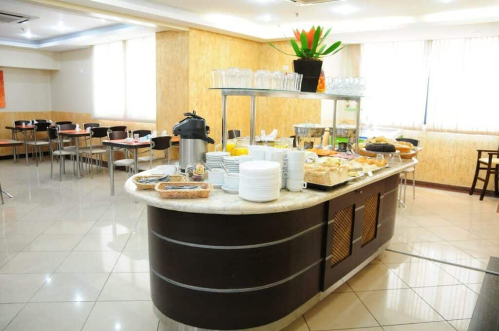 Um balcão com café da manhã variado da Brasília Santana Gold Flat. No fundo, mesas e cadeiras.