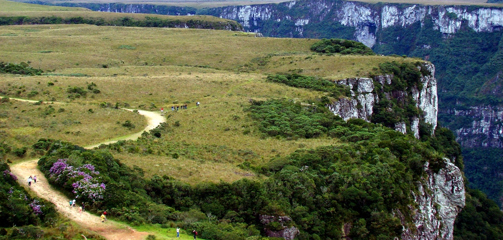Vista de cima do Cânion Fortaleza. Do lado esquerdo a trilha com pessoas, do lado direito a vista das montanhas.