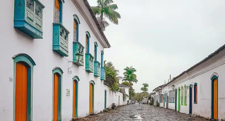 Uma rua de paralelepípedos repleta de edifícios coloridos em estilo colonial, com portas e janelas iluminadas em um dia nublado.