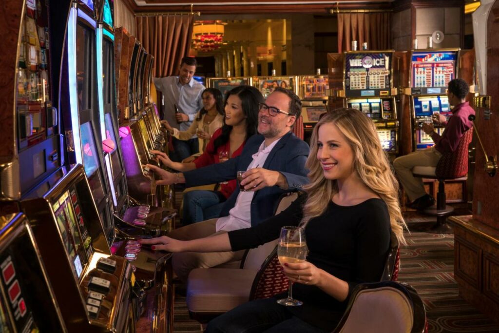 Pessoas jogando nas máquinas caça-níqueis do cassino do hotel Golden Nugget. Elas estão enfileiradas, todas olhando para a tela e apertando botões.