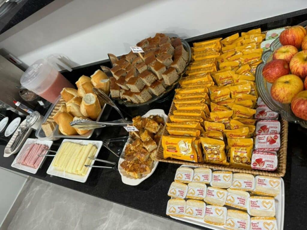 Um balcão com uma variedade do café da manhã, com pães, bolos, frios e biscoitos Bauduco à vontade