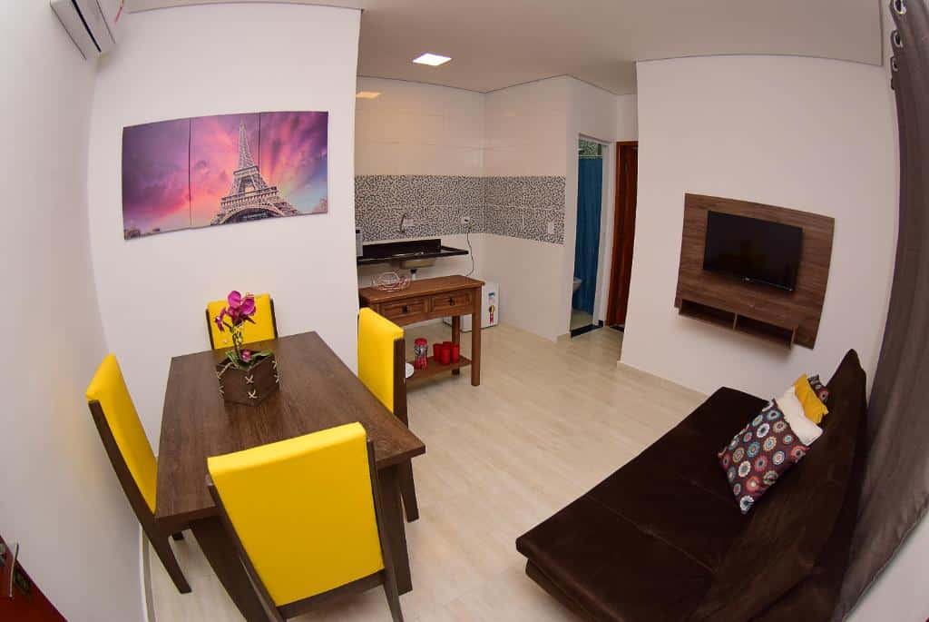Sala e cozinha do Hotel Numaz Brás. Do lado esquerdo uma mesa de jantar, do lado direito um sofá e um painel com TV. No fundo uma pequena cozinha.