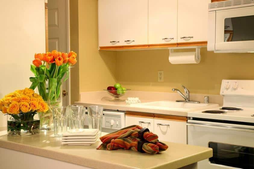 Cozinha no Jockey Club Suites. É possível ver armários, um fogão e uma pia. Logo em frente está um balção com copos, flores e panos de prato.