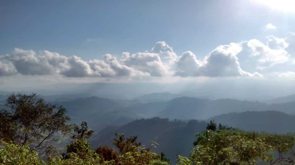 Foto tirada no Mirante Belvedere, ou Vista Chinesa, em Campos do Jordão, de onde é possível ver árvores e montanhas. O céu está com várias nuvens.