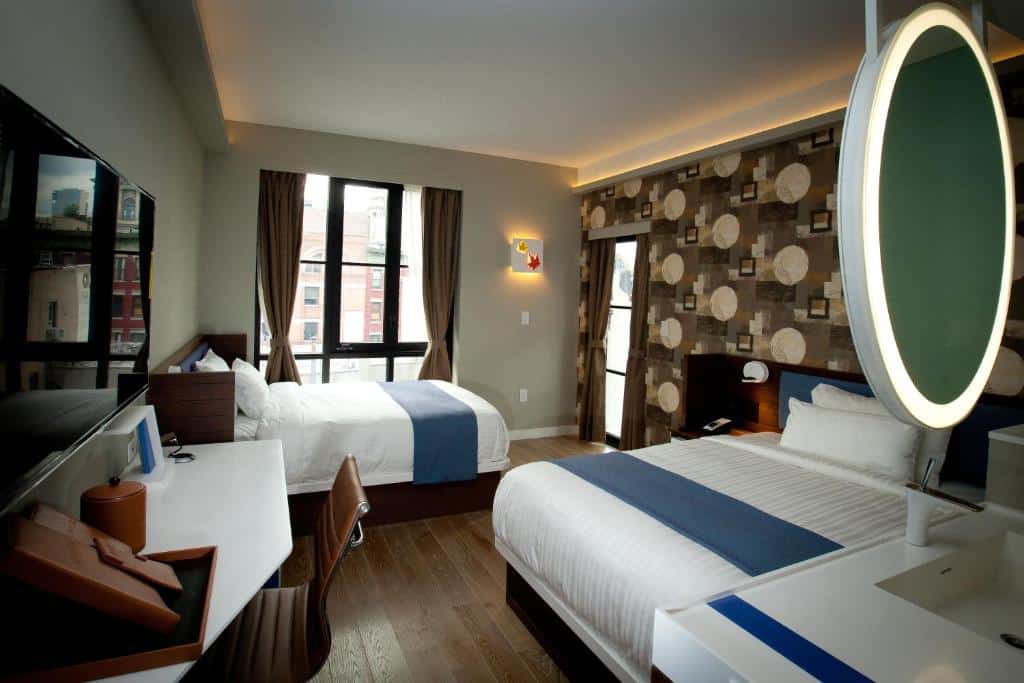 Um quarto do NobleDen hotel com duas camas de casal, uma grande janela com cortinas e uma decoração moderna. Há uma mesa de trabalho com uma cadeira e uma televisão de tela plana na parede. Este é um dos hotéis em Nova York.