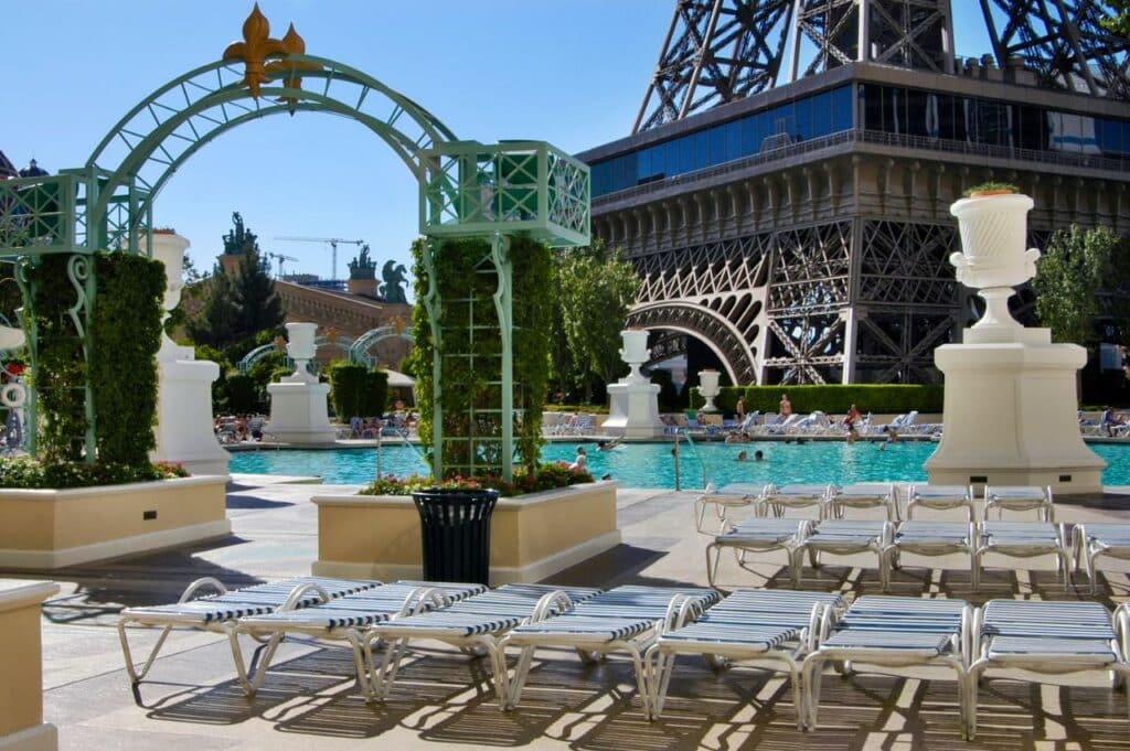 Piscina do Paris Las Vegas em frente a basa da torre eiffel. Um arco marca a entrada da piscina. Atrás dele estão várias espreguiçadeiras.