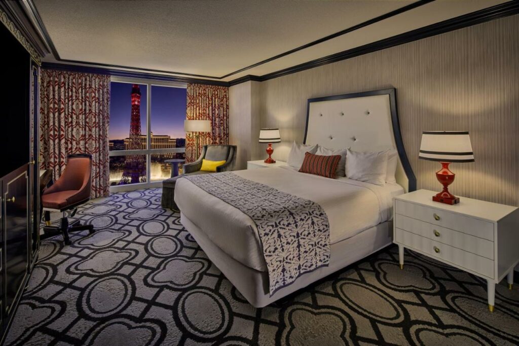 Quarto do Paris Las Vegas com uma cama de casal do lado direito, ao lado de uma mesinha com abajur. Do outro lado está uma grande janela e dois abajures.