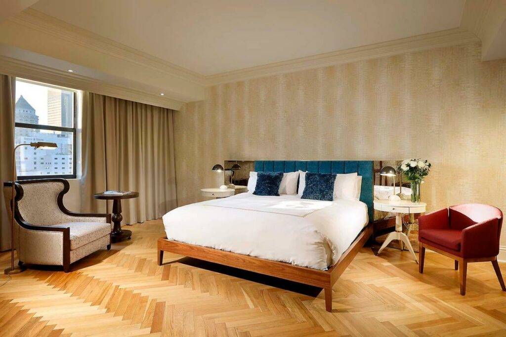 Um quarto do Eurostars Langford com uma cama grande, duas mesas laterais, uma cadeira e uma mesa pequena. Uma paisagem urbana é visível através da janela. Representa onde ficar em Miami.