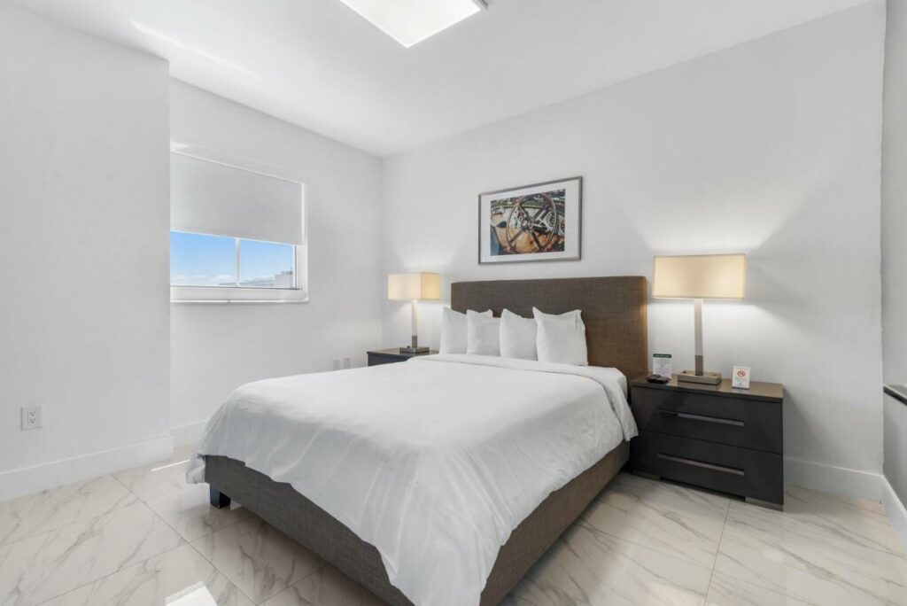 Quarto do Fortune House Hotel Suites com cama de casal no centro da imagem e em cada lado da cama uma cômoda com luminária. Representa melhores hotéis em Miami.
