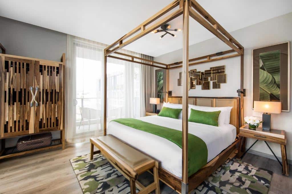 Quarto moderno do Lennox Miami Beach com cama de dossel, detalhes em verde, móveis de madeira e uma obra de arte geométrica acima da cama. Representa onde ficar em Miami.