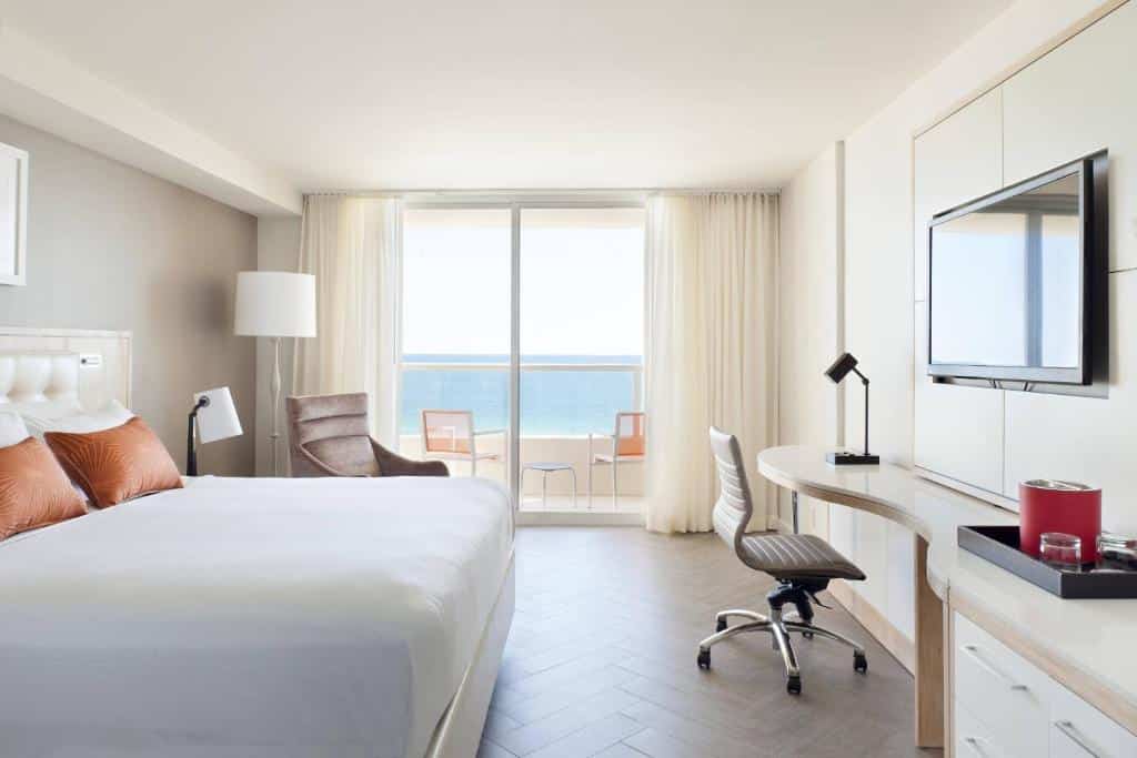 Quarto do Marriott Stanton South Beach com cama grande, escrivaninha, cadeira, TV e vista para o mar através de portas de vidro deslizantes que levam a uma varanda com assentos.