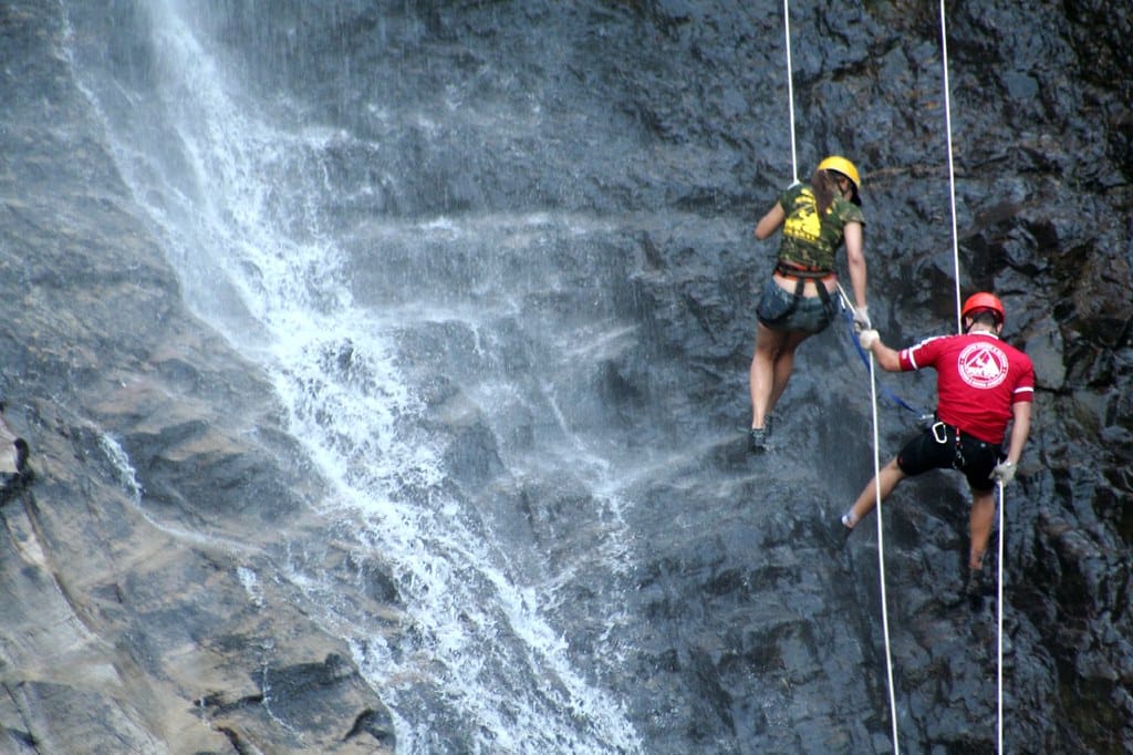 Um casal descendo de rapel no paredão da cachoeira.
