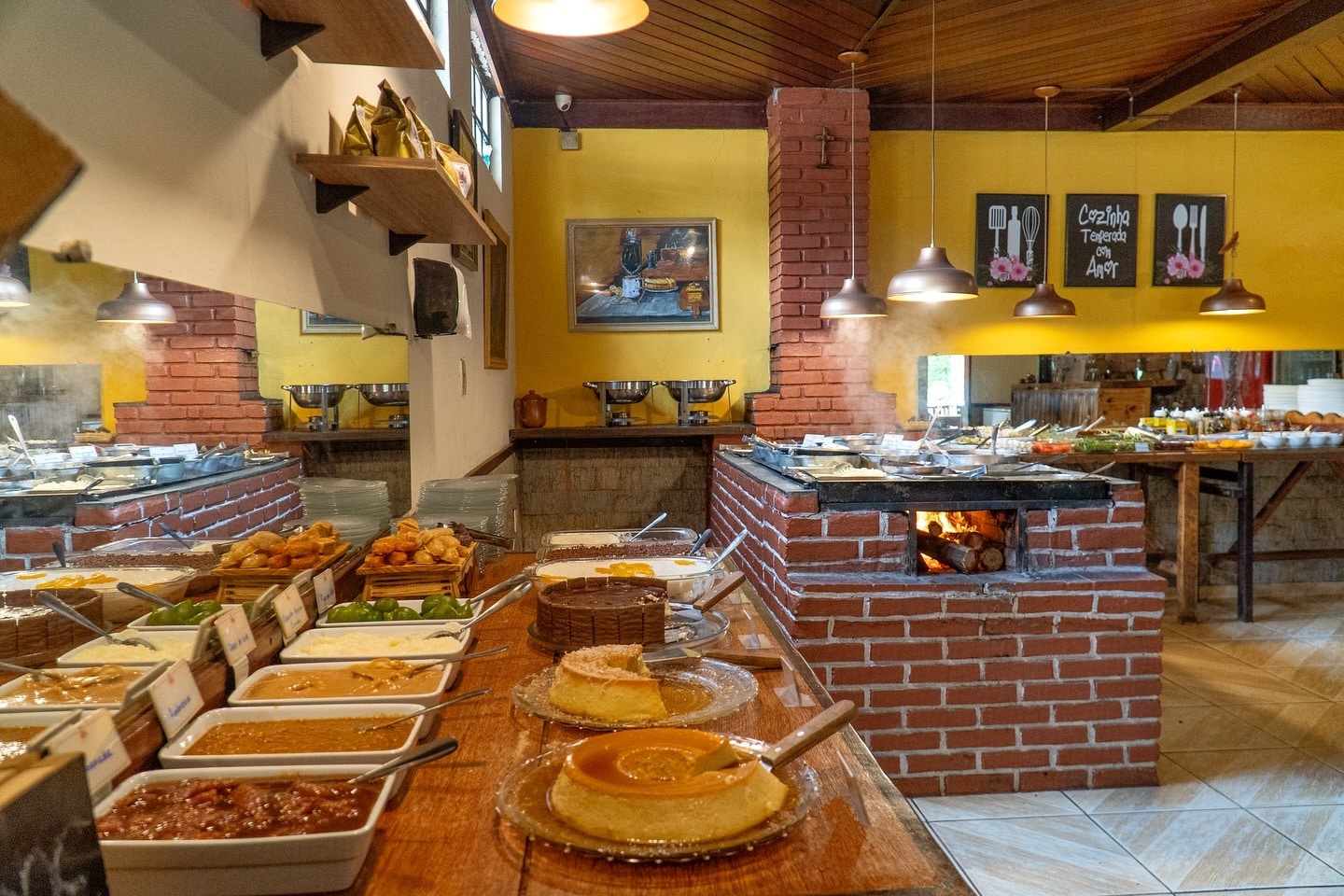 Parte do Restaurante Trem de Minas que mostra do lado esquerdo uma mesa com doces e ao fundo um fogão a lenha com mais comidas. Imagem ilustrando post O que fazer em Visconde de Mauá.