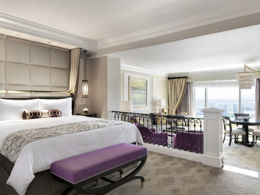 Quarto no The Venetian. Uma cama de casal está do lado esquerdo com um recamier, na parte mais alto do ambiente. Do lado direito está a parte mais baixa, depois de um degrau. Nessa área estão poltronas, mesas e uma janela gigante com vista para a cidade.