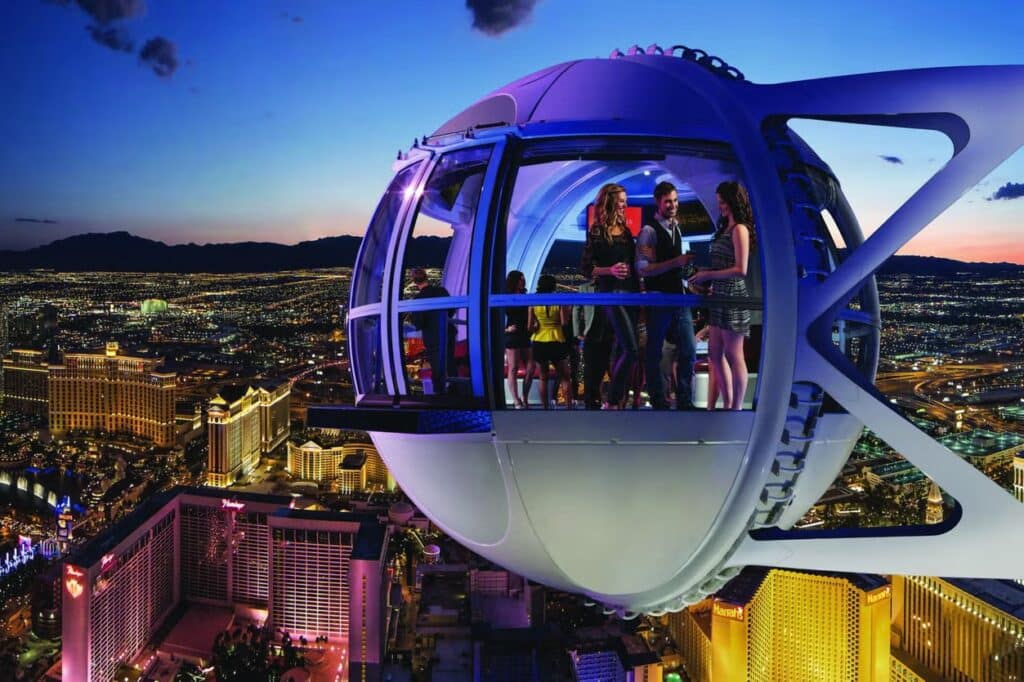 Um grupo de pessoas aprecia a vista da cidade da high roller em Las Vegas, uma roda gigante, com edifícios bem iluminados visíveis abaixo ao anoitecer.