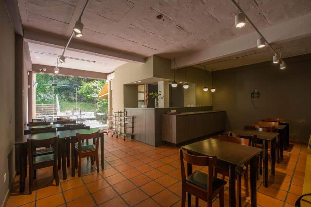 Área comum do Boutique Apartments Plaza Dorrego, um dos hotéis em San Telmo, Buenos Aires, com mesas e cadeiras quadradas em estilo moderno, há luminárias no teto e acima do balcão central, ao longo, é possível um ambiente aberto com vegetação.