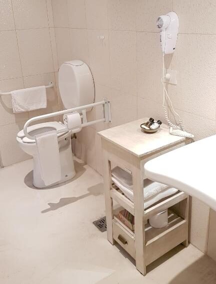 Banheiro do L'Adresse Hôtel Boutique, um dos hotéis em San Telmo, Buenos Aires, com adaptações para PcDs, como vaso sanitário com barras de apoio, cômoda móvel e prateleiras baixas.