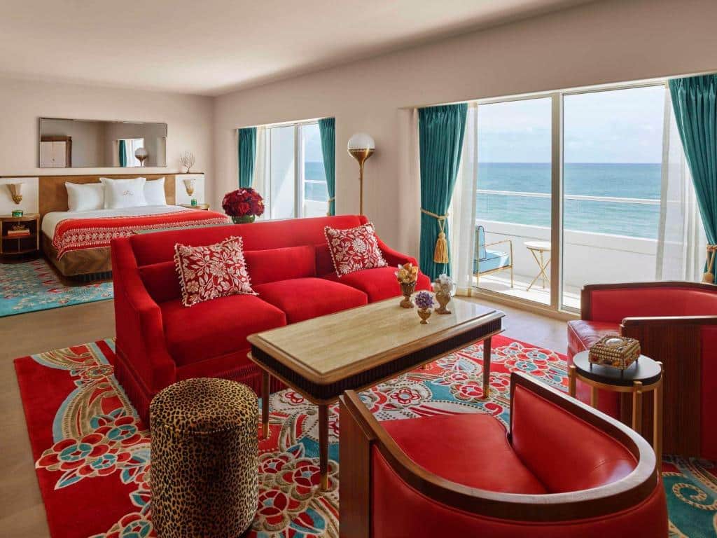 Quarto do Faena Hotel Miami Beach com sala de estar a frente com duas poltronas a frente no centro uma mesa e um sofá, atrás do sofá uma cama de casal. Representa hotéis para Brasileiros em Miami.