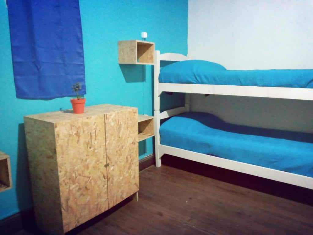 Quarto simples da Casa Copada. Uma cama beliche do lado direito, do lado esquerdo uma cômoda e duas prateleiras.