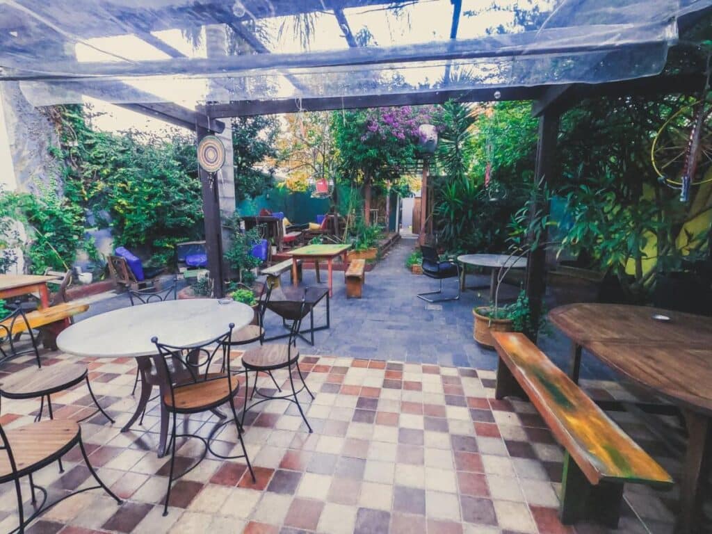 Área externa do Charruas, com diversas mesas e cadeiras, ao redor várias plantas. Imagem para ilustrar post sobre hostels em Montevidéu.